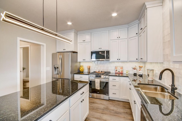 kitchen with appliances with stainless steel finishes, dark stone countertops, white cabinetry, and sink