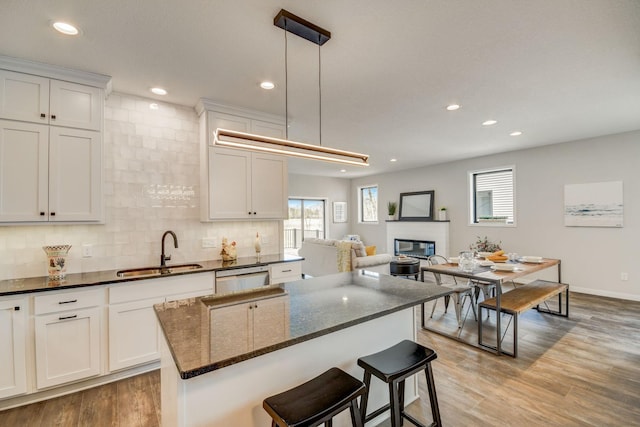 kitchen with decorative light fixtures, dishwasher, sink, white cabinetry, and light wood-type flooring