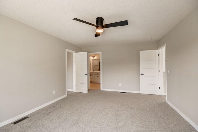 unfurnished bedroom featuring a textured ceiling, ensuite bathroom, ceiling fan, and carpet