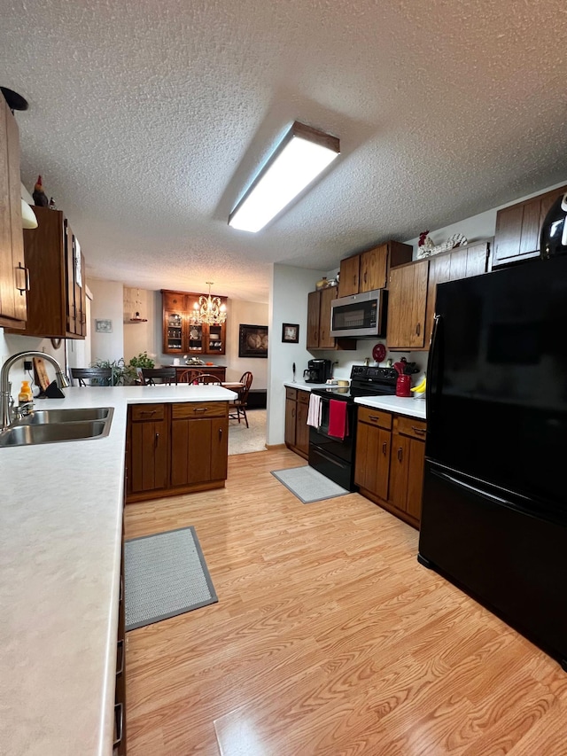 kitchen featuring light hardwood / wood-style flooring, a notable chandelier, a textured ceiling, decorative light fixtures, and black appliances