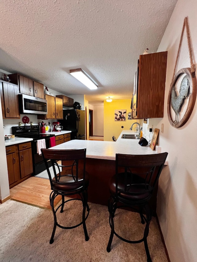 kitchen featuring kitchen peninsula, light wood-type flooring, a textured ceiling, sink, and black appliances