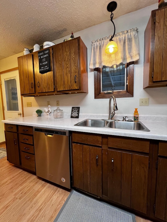 kitchen with sink, hanging light fixtures, light hardwood / wood-style flooring, stainless steel dishwasher, and a textured ceiling