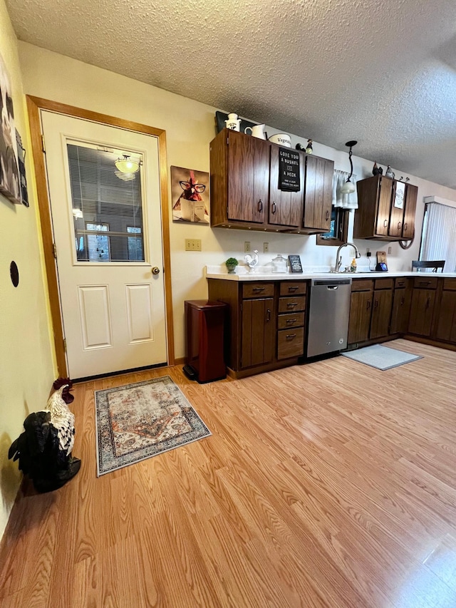 kitchen featuring hanging light fixtures, stainless steel dishwasher, light wood-type flooring, a textured ceiling, and dark brown cabinetry