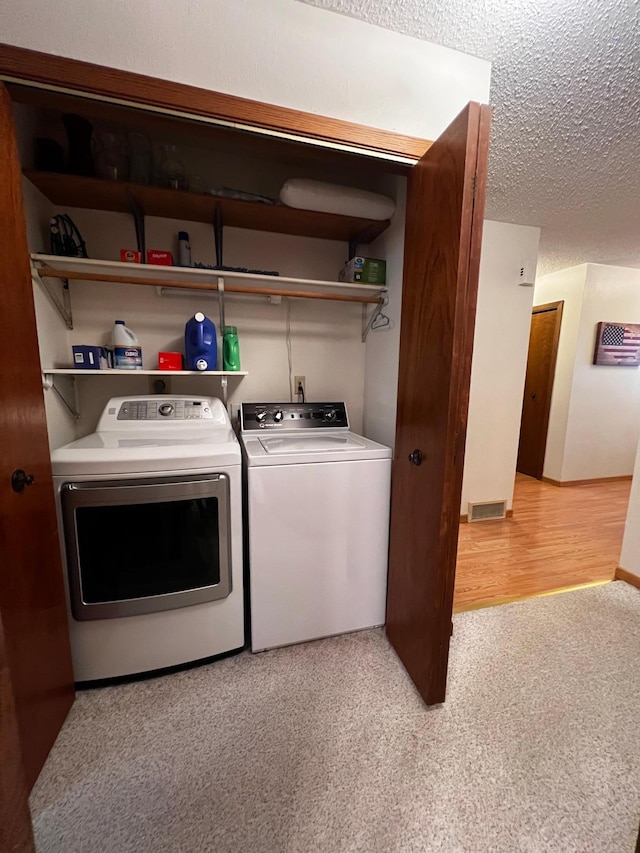 laundry area with a textured ceiling, light hardwood / wood-style flooring, and washing machine and clothes dryer