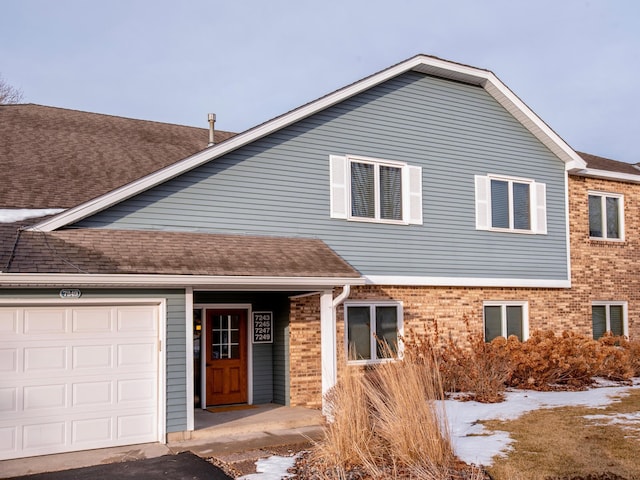 view of front of house featuring an attached garage, brick siding, and roof with shingles