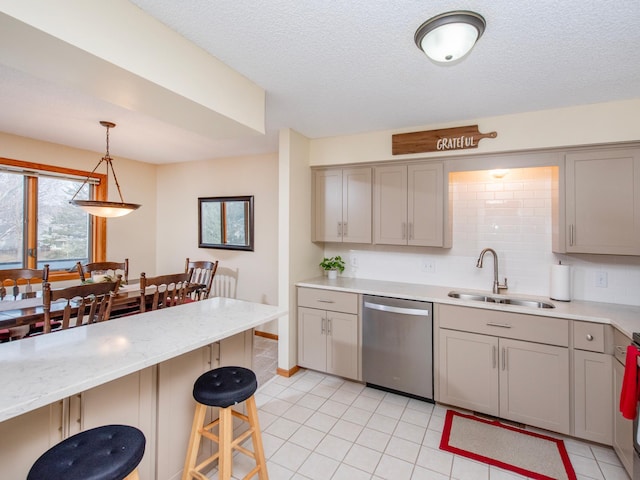 kitchen with a breakfast bar, gray cabinetry, a sink, backsplash, and dishwasher