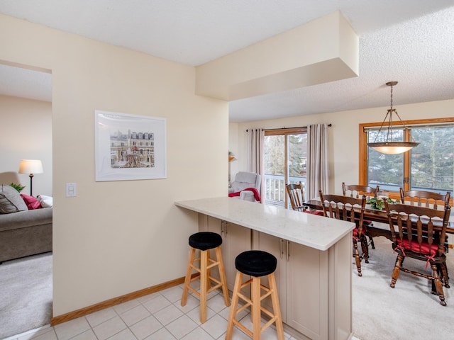 kitchen with a kitchen bar, decorative light fixtures, light stone counters, a peninsula, and baseboards