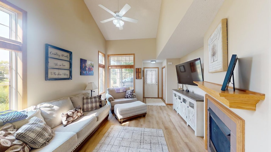 living room with ceiling fan, a tile fireplace, high vaulted ceiling, and light hardwood / wood-style flooring