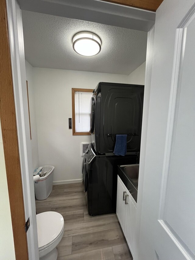 bathroom with a textured ceiling, stacked washer / dryer, hardwood / wood-style flooring, and toilet