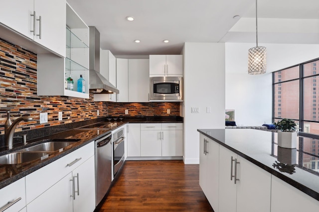 kitchen featuring a sink, decorative light fixtures, dark wood finished floors, appliances with stainless steel finishes, and wall chimney range hood