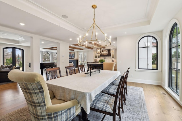 dining area with crown molding, a chandelier, a raised ceiling, and light hardwood / wood-style floors