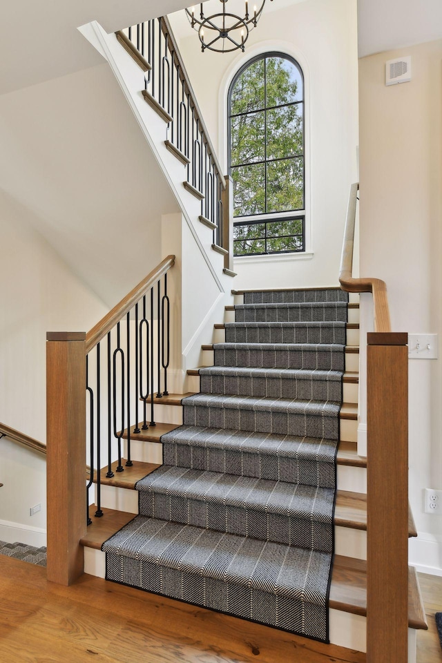 stairway featuring a high ceiling, hardwood / wood-style floors, and a notable chandelier