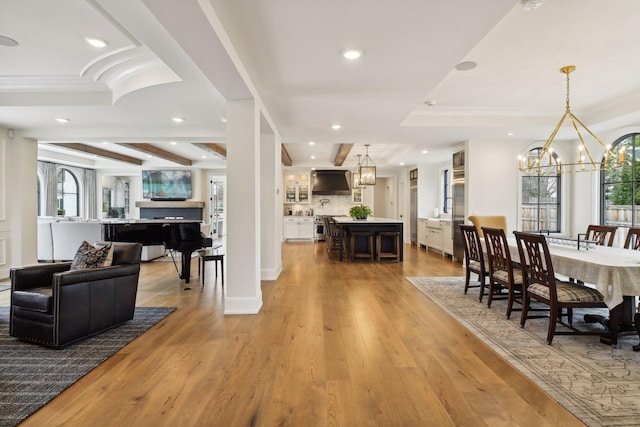 dining area featuring an inviting chandelier, beam ceiling, light hardwood / wood-style flooring, and a tray ceiling