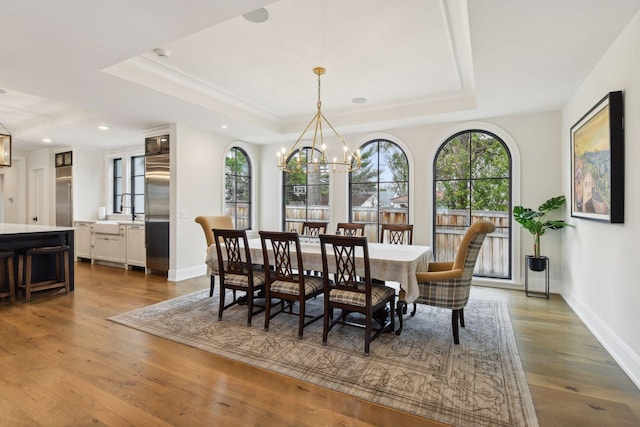 dining space with a healthy amount of sunlight, hardwood / wood-style floors, a notable chandelier, and a tray ceiling