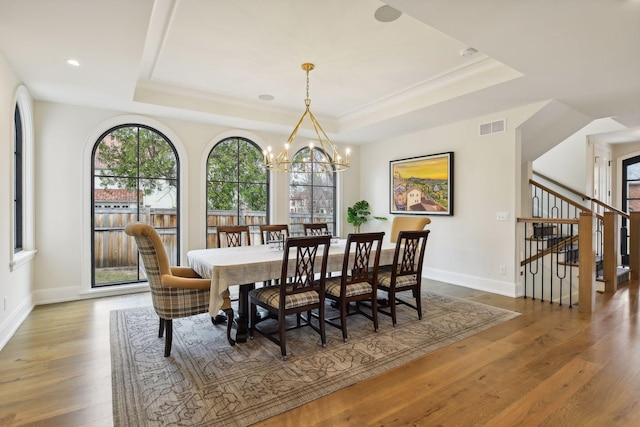 dining area with crown molding, a tray ceiling, wood-type flooring, and a chandelier