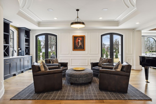 living room featuring crown molding, a tray ceiling, light hardwood / wood-style floors, and french doors