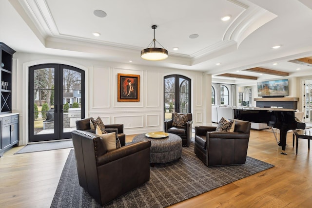 living room with french doors, a tray ceiling, light hardwood / wood-style floors, and crown molding