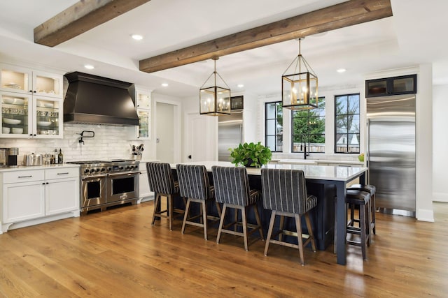 kitchen with a kitchen island, white cabinetry, premium appliances, custom exhaust hood, and hanging light fixtures