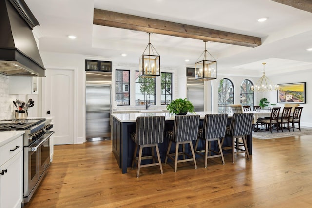 kitchen featuring pendant lighting, white cabinets, premium appliances, island exhaust hood, and a spacious island