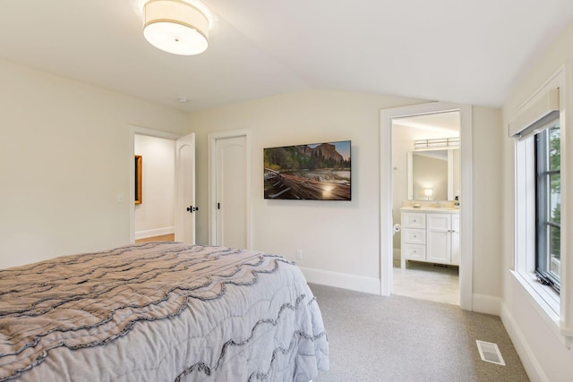 bedroom featuring light carpet, ensuite bath, and vaulted ceiling