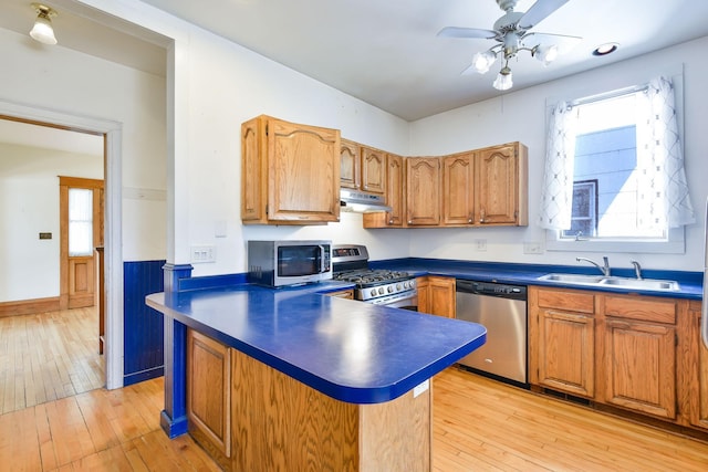 kitchen featuring dark countertops, light wood-style floors, under cabinet range hood, a sink, and appliances with stainless steel finishes