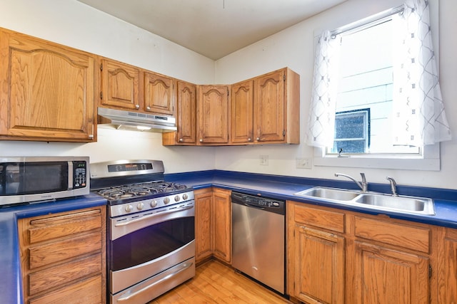 kitchen featuring brown cabinets, appliances with stainless steel finishes, a sink, light wood finished floors, and under cabinet range hood