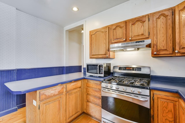 kitchen with light wood finished floors, appliances with stainless steel finishes, under cabinet range hood, and wallpapered walls