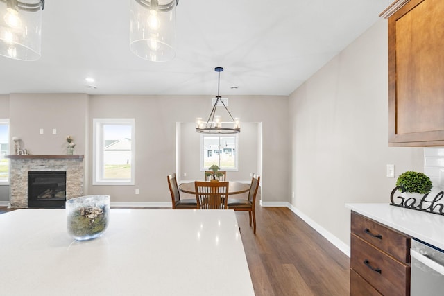 kitchen featuring a stone fireplace, dark hardwood / wood-style flooring, hanging light fixtures, an inviting chandelier, and stainless steel dishwasher