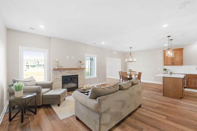 living room featuring light hardwood / wood-style floors, a stone fireplace, and a chandelier