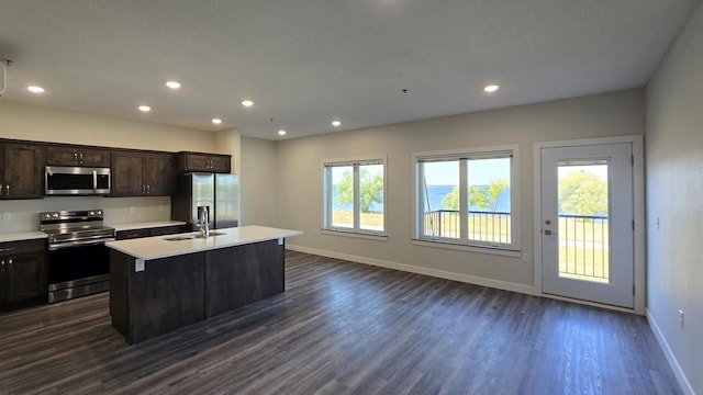 kitchen featuring appliances with stainless steel finishes, dark hardwood / wood-style flooring, sink, an island with sink, and dark brown cabinetry