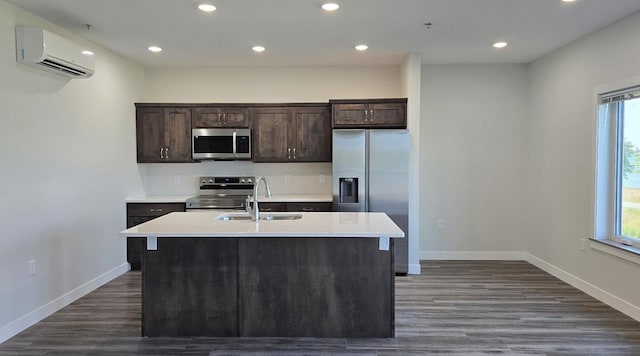 kitchen with stainless steel appliances, sink, dark wood-type flooring, a center island with sink, and an AC wall unit