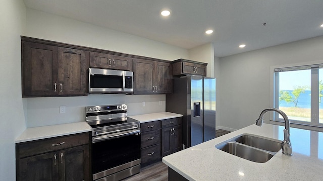 kitchen featuring light stone countertops, stainless steel appliances, sink, dark hardwood / wood-style floors, and dark brown cabinetry