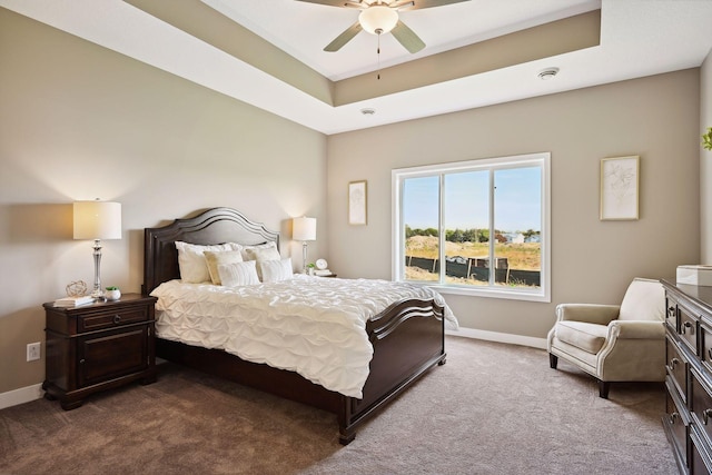 carpeted bedroom with a raised ceiling and ceiling fan