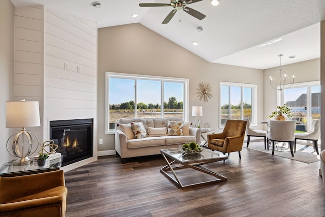 living room with ceiling fan with notable chandelier, dark hardwood / wood-style flooring, high vaulted ceiling, and a large fireplace