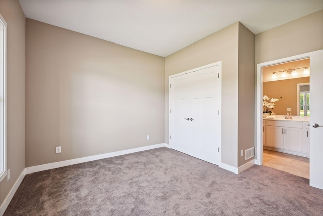 unfurnished bedroom with sink, ensuite bathroom, and light colored carpet