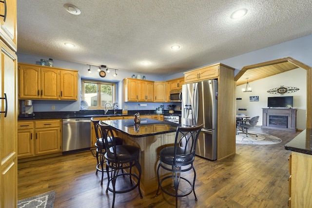 kitchen with a center island, appliances with stainless steel finishes, dark wood-type flooring, and a breakfast bar