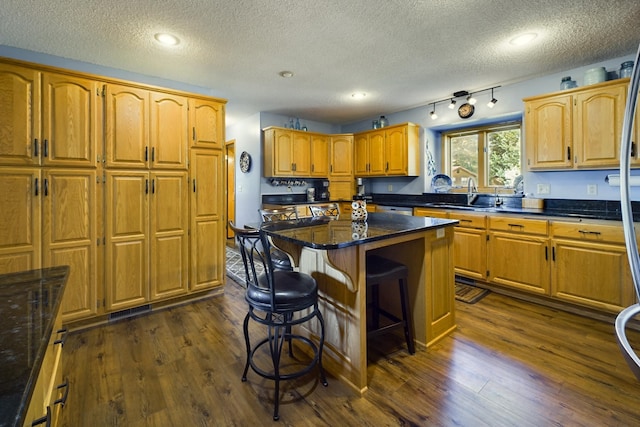 kitchen with sink, dark wood-type flooring, a breakfast bar area, and a kitchen island