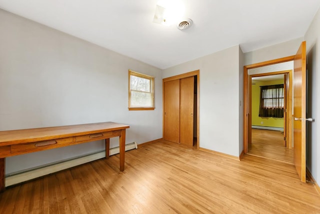 bedroom featuring a closet, baseboard heating, and light hardwood / wood-style flooring