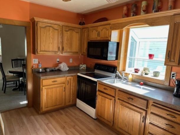 207 6th St, Montevideo, MN 56265 - kitchen featuring electric stove, black microwave, light wood-style floors, and brown cabinetry
