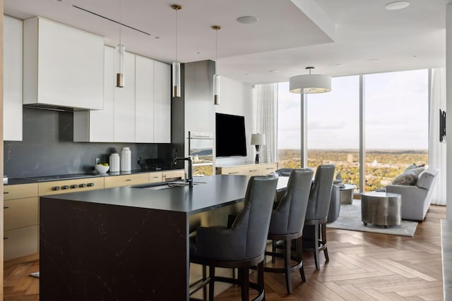 kitchen featuring parquet flooring, a kitchen island with sink, white cabinetry, and tasteful backsplash