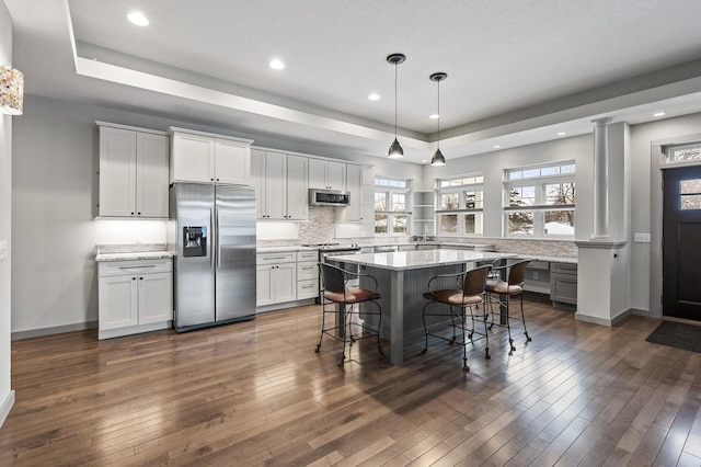 kitchen with a kitchen bar, ornate columns, white cabinetry, hanging light fixtures, and stainless steel appliances