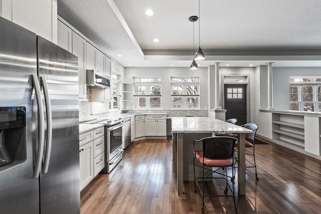 kitchen with a breakfast bar area, white cabinetry, light stone counters, decorative light fixtures, and stainless steel appliances