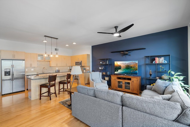 living room featuring ceiling fan, sink, and light wood-type flooring