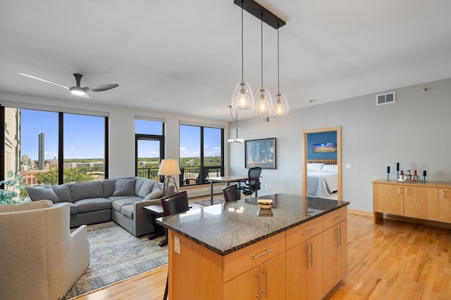 kitchen with a wealth of natural light, light hardwood / wood-style flooring, ceiling fan, and dark stone countertops