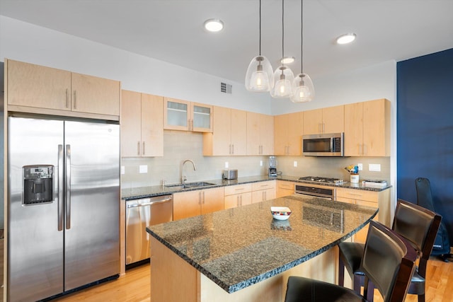 kitchen with a center island, stainless steel appliances, dark stone countertops, and light brown cabinets