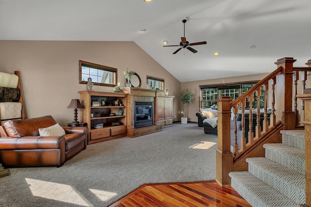 living room with a fireplace, a ceiling fan, high vaulted ceiling, light wood-type flooring, and stairs