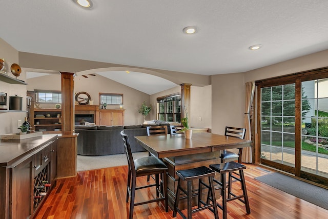 dining space featuring a wealth of natural light, arched walkways, a glass covered fireplace, and ornate columns