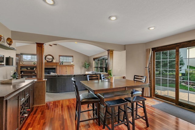 dining room with a wealth of natural light, a glass covered fireplace, decorative columns, and lofted ceiling