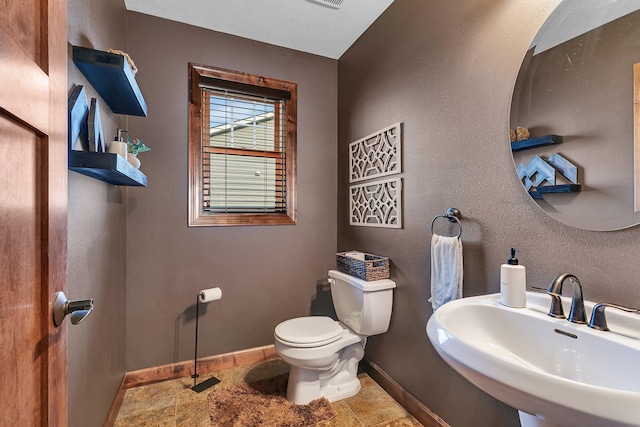 bathroom featuring visible vents, baseboards, a textured wall, toilet, and a sink