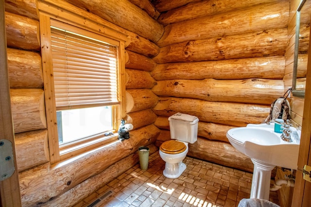 bathroom with toilet, rustic walls, and a healthy amount of sunlight